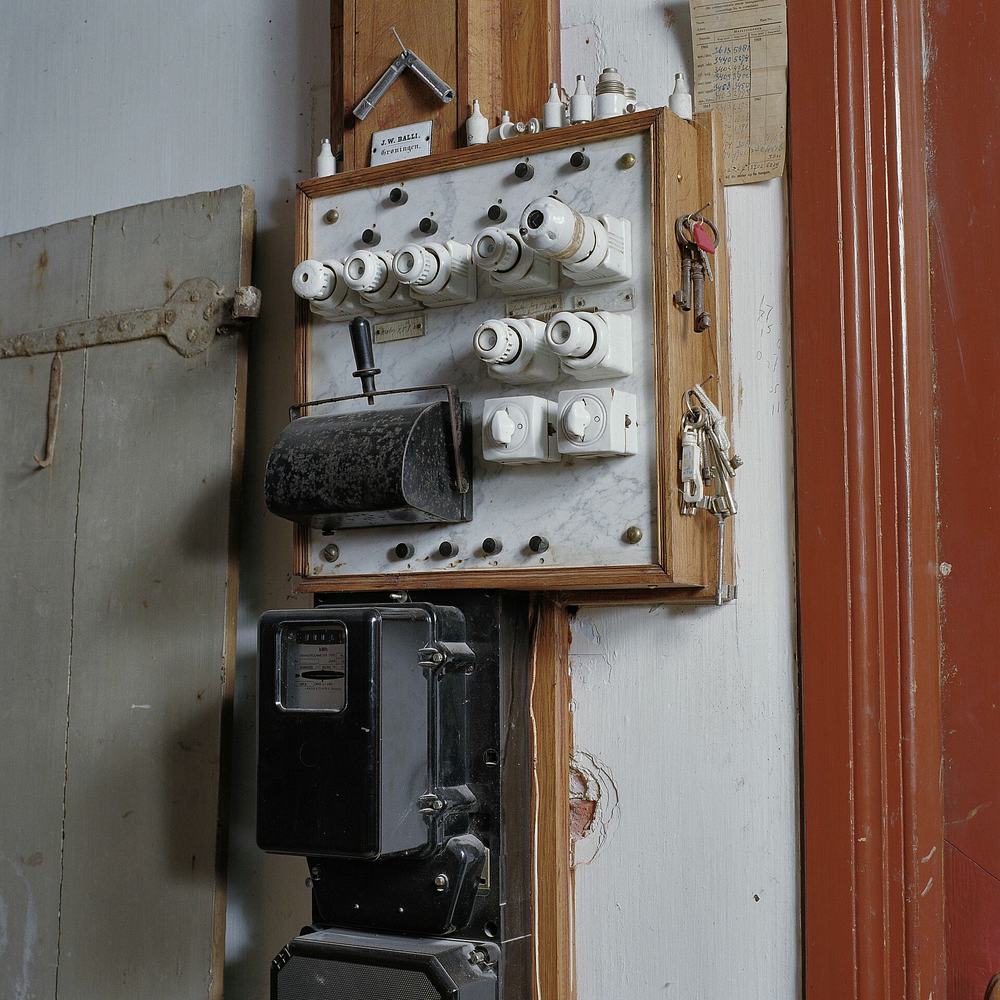 Een oude zekeringkast op een houten plank met porseleinen smeltzekeringen en een oude meter