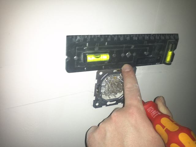 Een hand met een schroevendraaier zet een inbouwschakelaar vast, met een waterpas erop